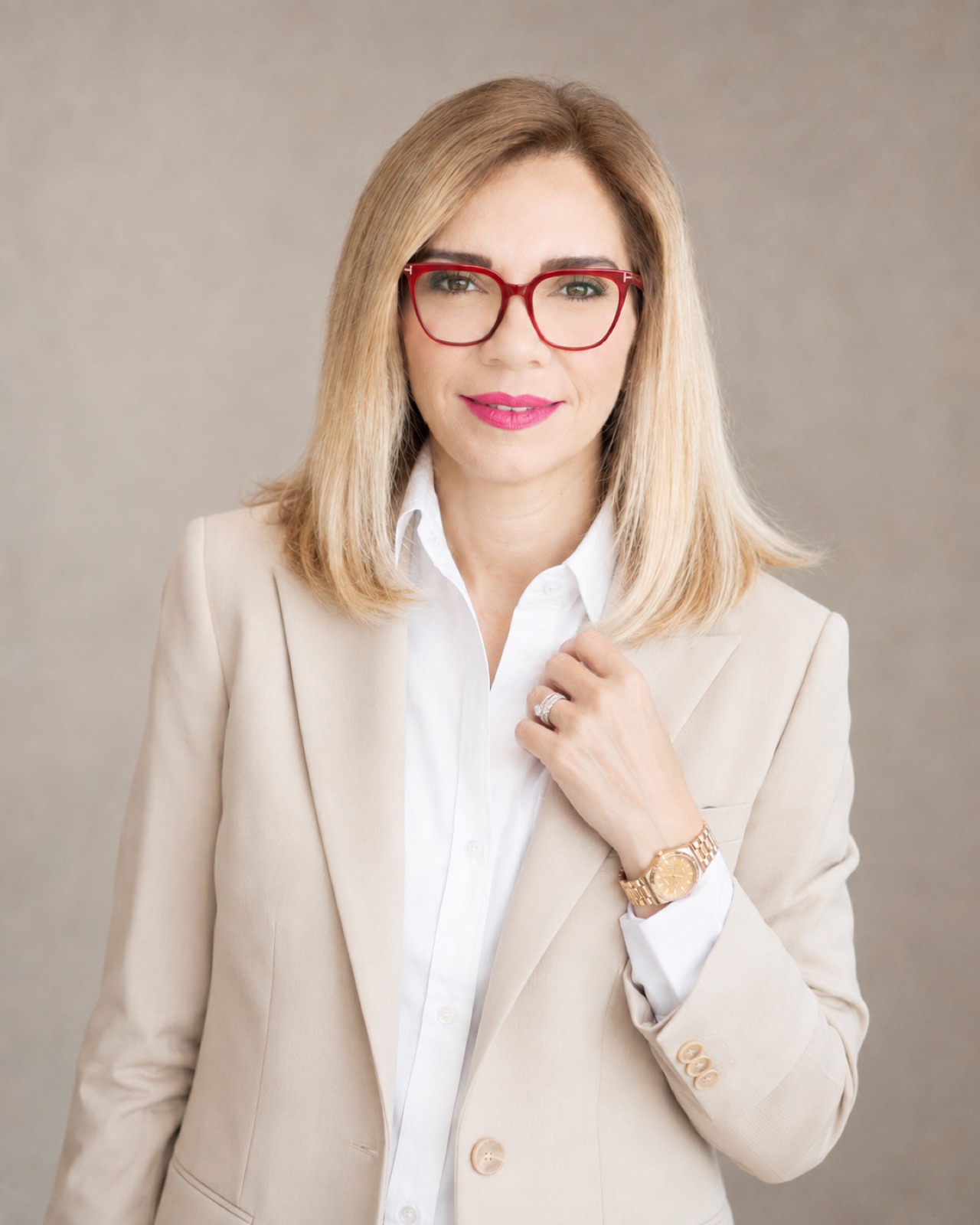Sand blazer, red frames. Hand at the lapel.